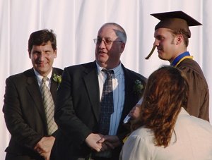 Assistant Superintendent Dr. Michael Bjalobok looks on as School Board member Ron Lang grants a diploma to his son David.